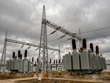 Wide-angle dramatic shot of a modern high-voltage power substation under an overcast, moody sky, steel structures and heavy electrical transformers.