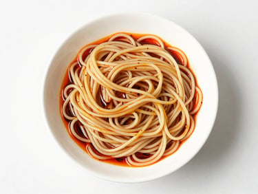 Bright overhead shot of hand-pulled Szechuan noodles in a white bowl, glistening oil, natural daylight