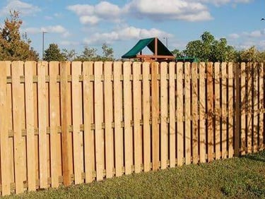 A brown wooden privacy fence installed in a backyard lawn near a playground set.