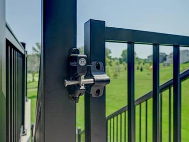 Close-up of a lockable black metal safety latch on a backyard deck gate for pool security.