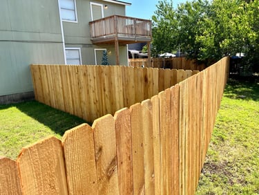 Newly installed cedar wood privacy fence in a residential backyard with green grass and a house balcony.