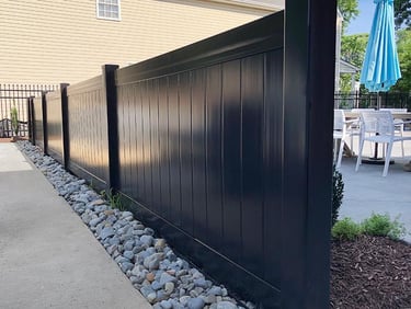 A modern black vinyl privacy fence installed alongside a backyard patio in Townsend DE