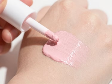 Close-up of liquid pink highlighter drops on smooth skin, soft natural sunlight, dewy skin texture