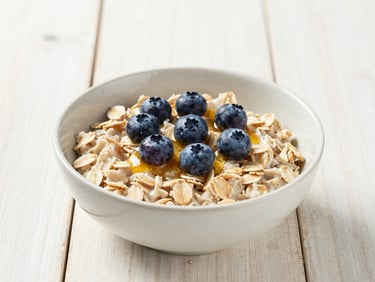 A simple ceramic bowl of warm steel-cut oatmeal topped with fresh blueberries and a drizzle of honey, rustic wooden table, bright morning light