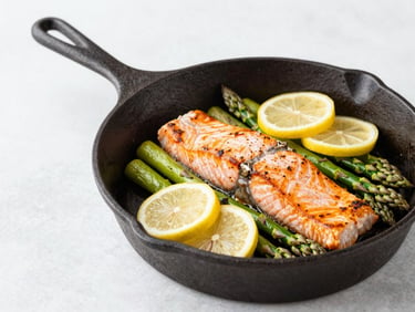 A rustic cast iron skillet with a baked salmon fillet surrounded by roasted asparagus spears and lemon slices, natural lighting.