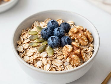 Overhead shot of a ceramic bowl filled with warm steel-cut oats, fresh wild blueberries, pumpkin seeds, and raw walnuts in soft daylight.