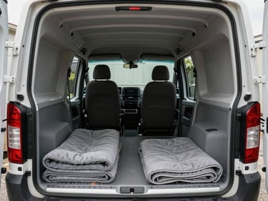 Interior of a compact cargo van, natural daylight entering from rear doors, padded blankets folded on the floor, clean empty load area showing modest volume, close perspective from driver-side loading edge