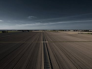 High-angle view of vast, structured agricultural fields with geometric irrigation channels under a dramatic, high-contrast sky