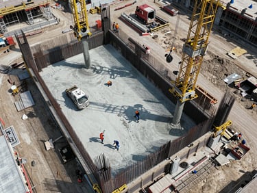Bird's-eye aerial photograph of an active construction site in Istanbul, steel reinforcement and concrete pours visible, workers small in frame dwarfed by the structure scale, bright even daylight, no filters