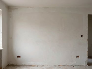 Wide shot of an unpainted apartment wall showing raw plaster patches, scuffs and old paint peeling at edges, natural window light, no people, before-state documentation