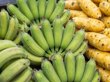 Close-up of a neatly arranged pile of fresh, vibrant green plantains and yellow yams, warm natural daylight, rich saturated colors, shallow depth of field