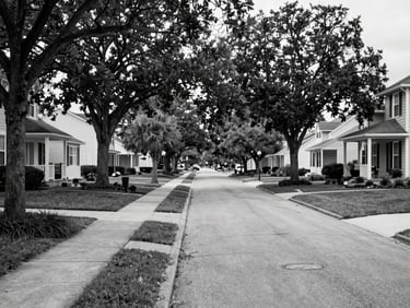 Black and white environmental shot of a tree-lined residential boulevard in North Myrtle Beach, single-family homes set back from wide sidewalks, natural daylight, quiet suburban framing