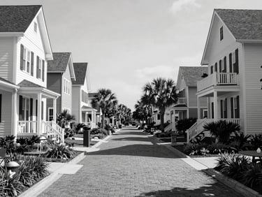 Black and white architectural shot of upscale homes in Market Common Myrtle Beach, pedestrian streetscape, brick-lined walkways, natural daylight, wide environmental framing