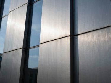 Close-up detail of a modern brushed steel facade reflecting a blue sky, high contrast geometric lines, sharp shadows.