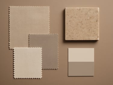 Overhead flat-lay of a design materials arrangement — fabric swatches, a stone sample tile, and a small color card on a warm taupe surface, even soft studio lighting, no hands or people