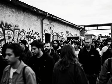 High contrast black and white photo, direct harsh flash, wide-angle 28mm lens, showing a crowded, raw pop-up store opening in a derelict industrial building, with blurred faces and bold graffiti.