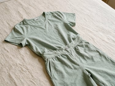 A flat lay of a minimalist sage green co-ord set on natural linen, warm diffused morning daylight, editorial style.