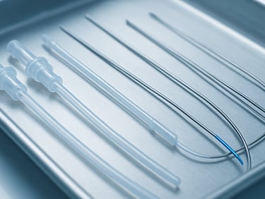 Macro clinical shot of sterile surgical catheters and medical guidewires on a metal tray, bright sterile lighting