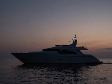 Wide-angle shot of a custom superyacht hull cutting through calm twilight waters, minimalist silhouette against a dark sky, natural low-key lighting.