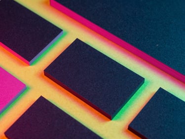 Vibrant flat-lay of corporate stationery, business cards with pink edge painting on dark paper, high-contrast colorful backlighting, sharp macro focus