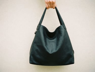 Hands holding a soft, unbranded black leather bag, warm diffused daylight