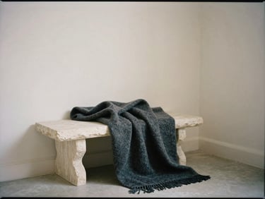 Architectural corner of an empty studio with a heavy cashmere throw draped over a stone bench