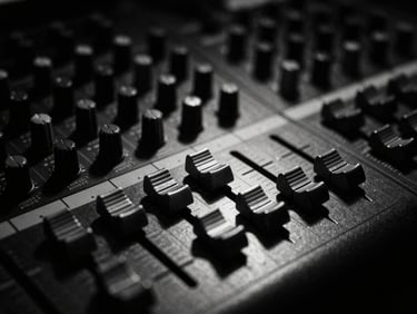 Extreme close-up of analog studio mixing console in deep shadow, single harsh cold metallic light reflecting on faders, desaturated monochrome, 35mm film grain