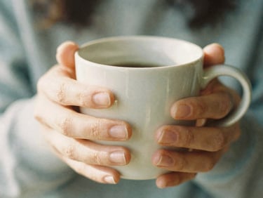 Close-up detail of hands holding a warm ceramic mug, soft morning light, shallow depth of field, 35mm film