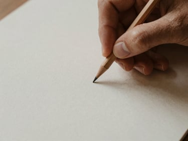 Close-up of hands holding a wooden pencil over a clean sheet of heavy-grain paper, soft diffused morning light, warm tones, quiet editorial style