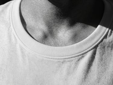 Tight macro crop of a t-shirt neckline, showing the reinforced stitching and fabric structure, harsh direct sunlight, deep shadows, monochrome black and white, 35mm film
