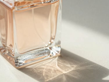 Heavy-weight glass perfume bottle refracting soft golden-hour window light, casting gentle organic shadows on an ivory surface, macro close-up, shallow depth of field, 35mm
