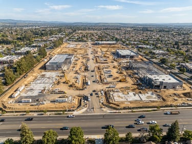 Wide-angle shot of a commercial plot development adjacent to a main road, showing construction progress and clear demarcations.