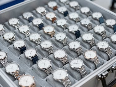 Close-up of organized rows of precision wristwatches in a secure distribution case, bright neutral commercial lighting