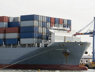 A large cargo container vessel docked at a structured modern port terminal, organized shipping containers stacked in neat grids, cool slate tones, daylight