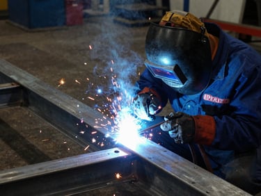 A certified welder in protective gear welding a large steel frame, bright blue welding arc, warm sparks, high contrast, sharp focus