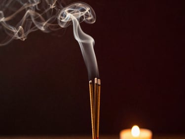 Close-up of natural incense smoke rising in a dark, atmospheric room, soft warm light illuminating the trails.