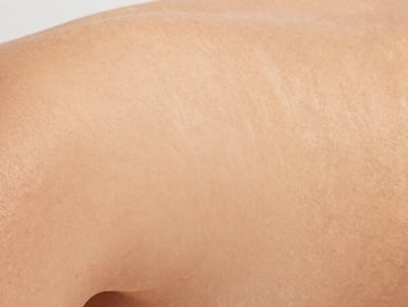Close-up of real, glowing skin with natural texture, soft daylight with warm undertones, clean minimalist composition