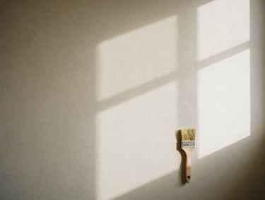 A freshly painted wall in a warm, neutral color, with soft shadows from a window, a painter's clean brush resting nearby, cozy domestic interior.