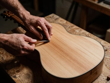 Hands of a luthier polishing a cypress wood guitar back, high contrast, warm workshop light