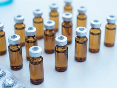 Close-up of sealed amber pharmaceutical bottles and blister packs on a clean sterile white surface, cool blue lighting.