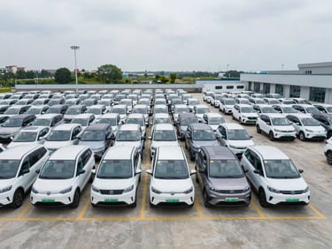 Wide-angle overhead shot of a commercial electric vehicle fleet yard under clean overcast daylight, vehicles parked in neat rows.