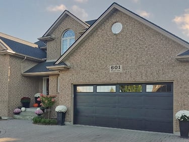Modern two-story brick home featuring a sleek dark gray double garage door and autumn floral decor.