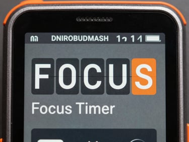 Close-up macro shot of DNIROBUDMASH Focus Timer app interface on a rugged Android device, showing a countdown, monospaced font, harsh fluorescent lighting, desaturated metallic tones, safety orange accents, flat lay.