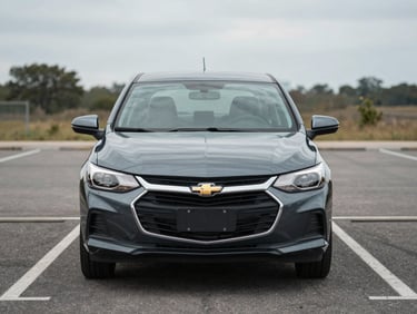 Front view of a dark gray Chevrolet Onix sedan parked straight-on in a daylight parking lot, overcast lighting, clean asphalt