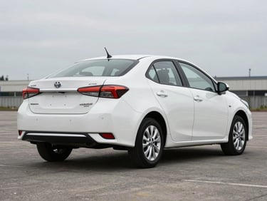 Three-quarter rear view of a white Toyota Yaris sedan on a clean daylight lot, overcast sky, minimal background detail