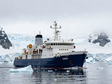 An ice-strengthened expedition vessel navigating calm waters filled with small icebergs in Antarctica, dramatic glaciers in background