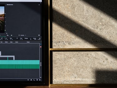 Symmetrical flat lay composition, hard architectural shadows, dramatic side-lighting. A split-screen showing a digital video editing timeline on the left and a raw concrete wall with brass accents on the right, 35mm