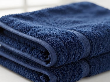 Tight macro close-up of a folded navy blue 700 GSM bath towel, showcasing its thick, dense loop pile and hem stitching, soft natural window light, crisp whites and deep navy tones, shallow depth of field, 35mm