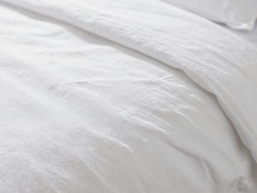 Macro close-up of crisp white long-staple combed cotton bed sheet texture, showing fine weave and subtle sheen, soft natural window light, crisp whites and deep navy tones, shallow depth of field, 35mm