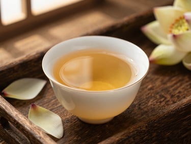 Close-up of a delicate porcelain cup filled with clear golden lotus tea, fresh lotus petals scattered on a rustic wooden tray, soft warm lighting